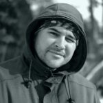 Portrait of a man in a hoodie smiling warmly, with a blurred outdoor winter background.