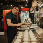 Adult man in an apron working with dough in a bakery kitchen.