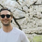 Happy man in sunglasses enjoying a sunny day amidst blooming cherry blossoms.