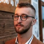 Confident young man with glasses in a stylish suit posing outdoors.